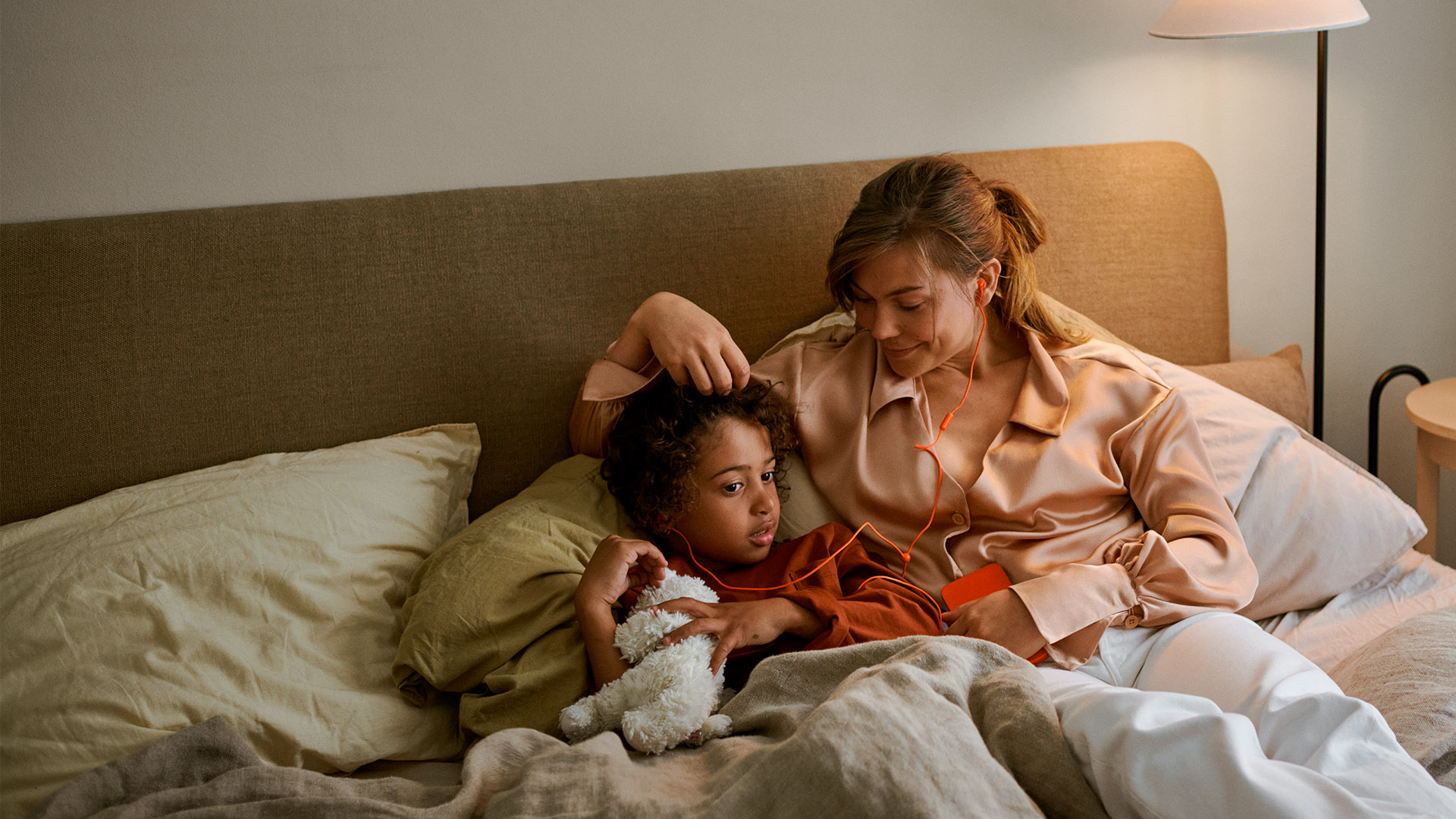 En kvinde med barn hører lydbog i sengen